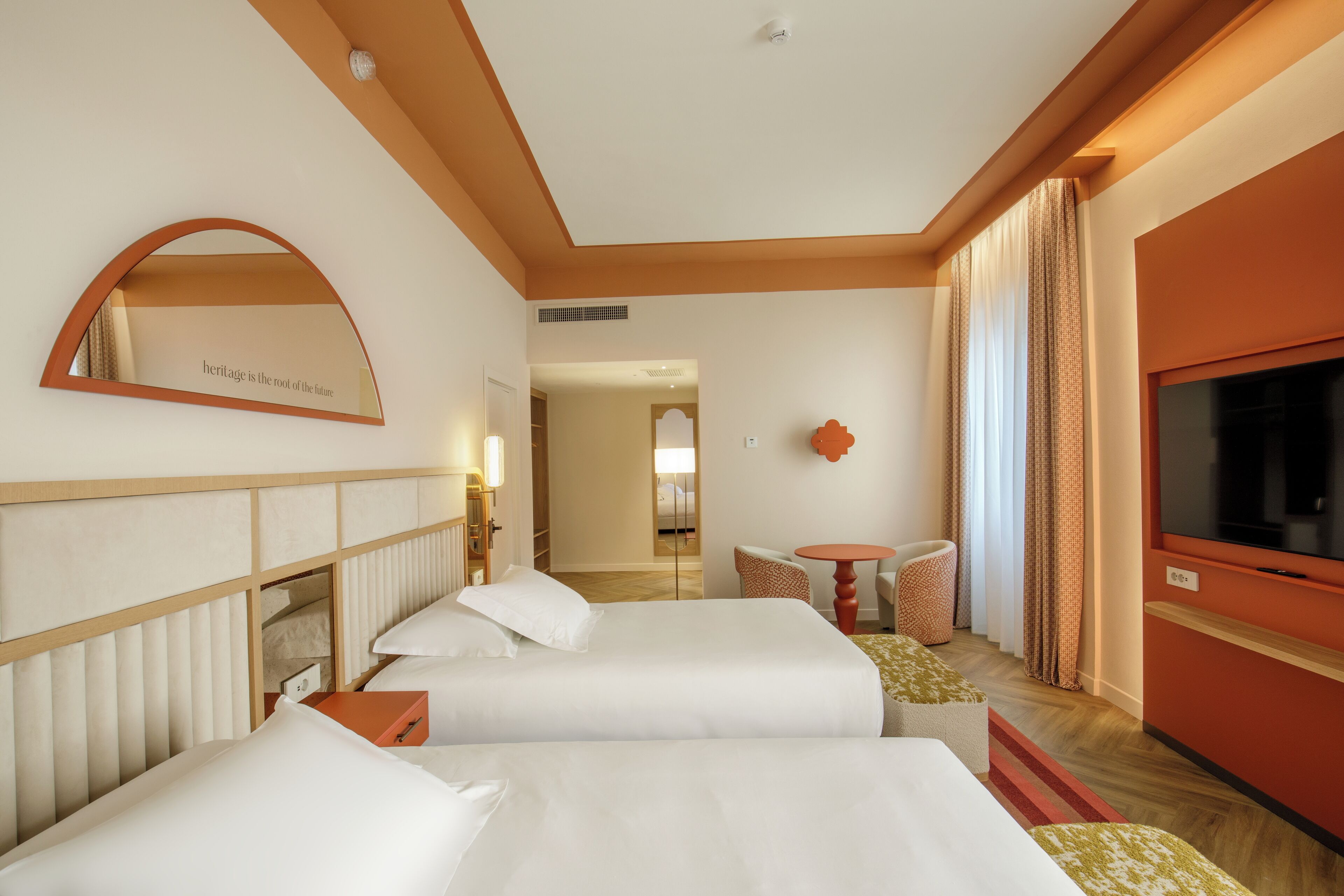 Habitación de hotel con dos camas, un televisor, una mesita y un espejo con una cita.