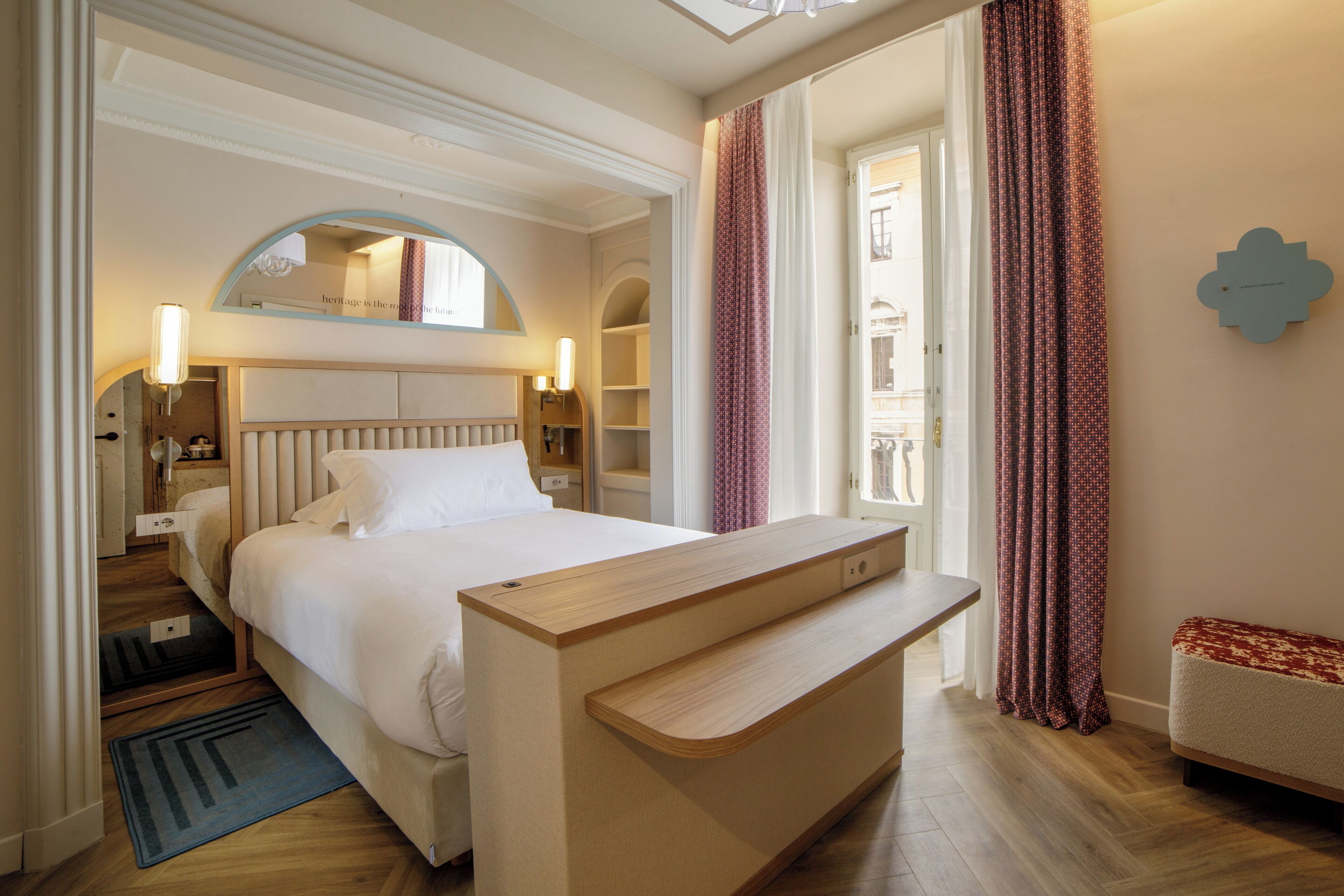 Una camera d'albergo con un letto, un comodino, uno specchio e vista esterna.