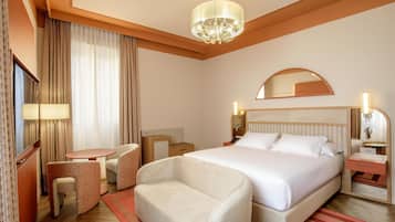 A hotel room with a bed, bedside tables, a desk, a chair, a mirror, and a chandelier.