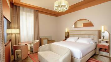 A hotel room with a bed, bedside tables, a chair, a desk, a mirror, and a chandelier.