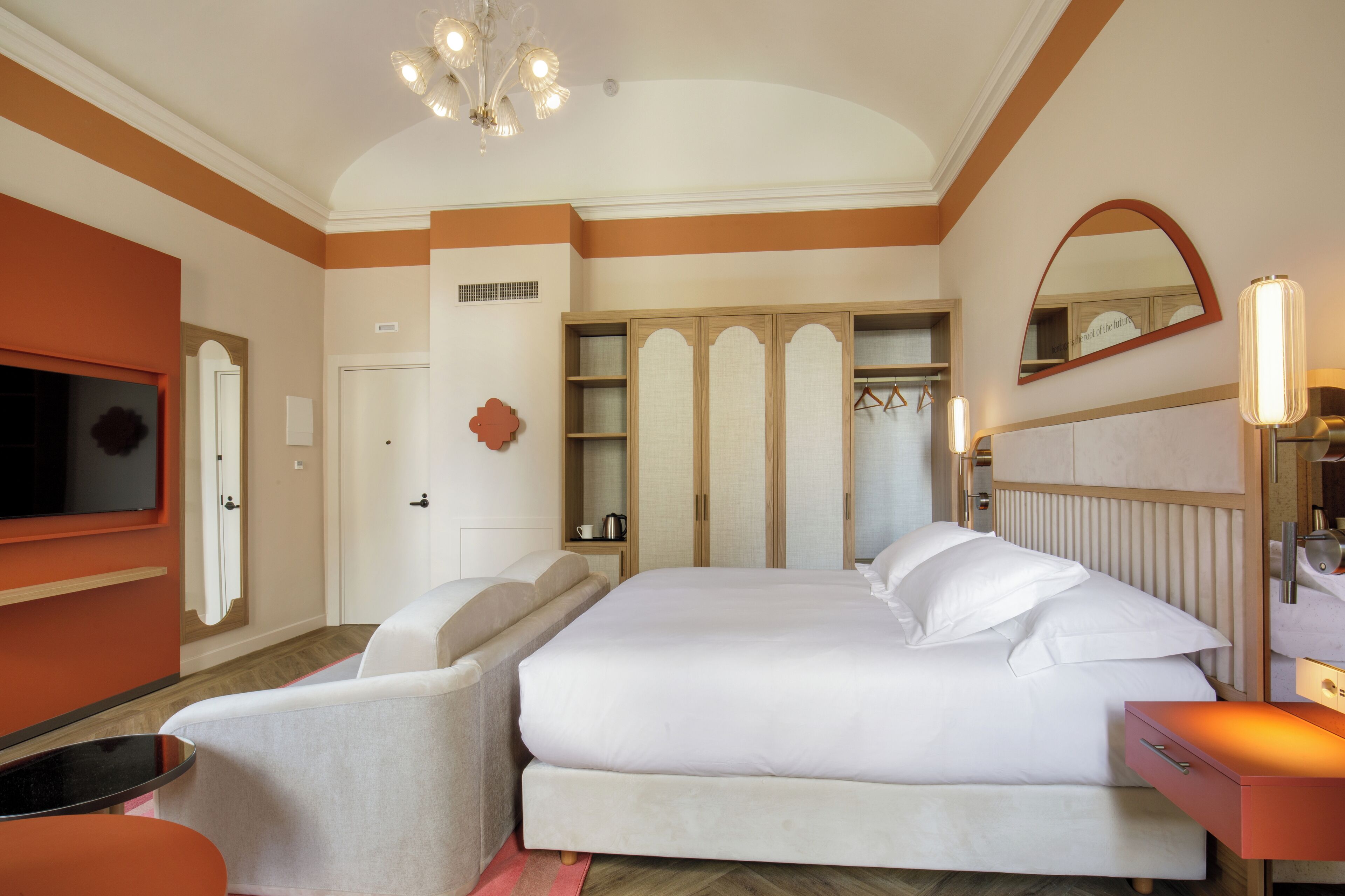 A hotel room with a large bed, a TV, a seating area, and a wardrobe.