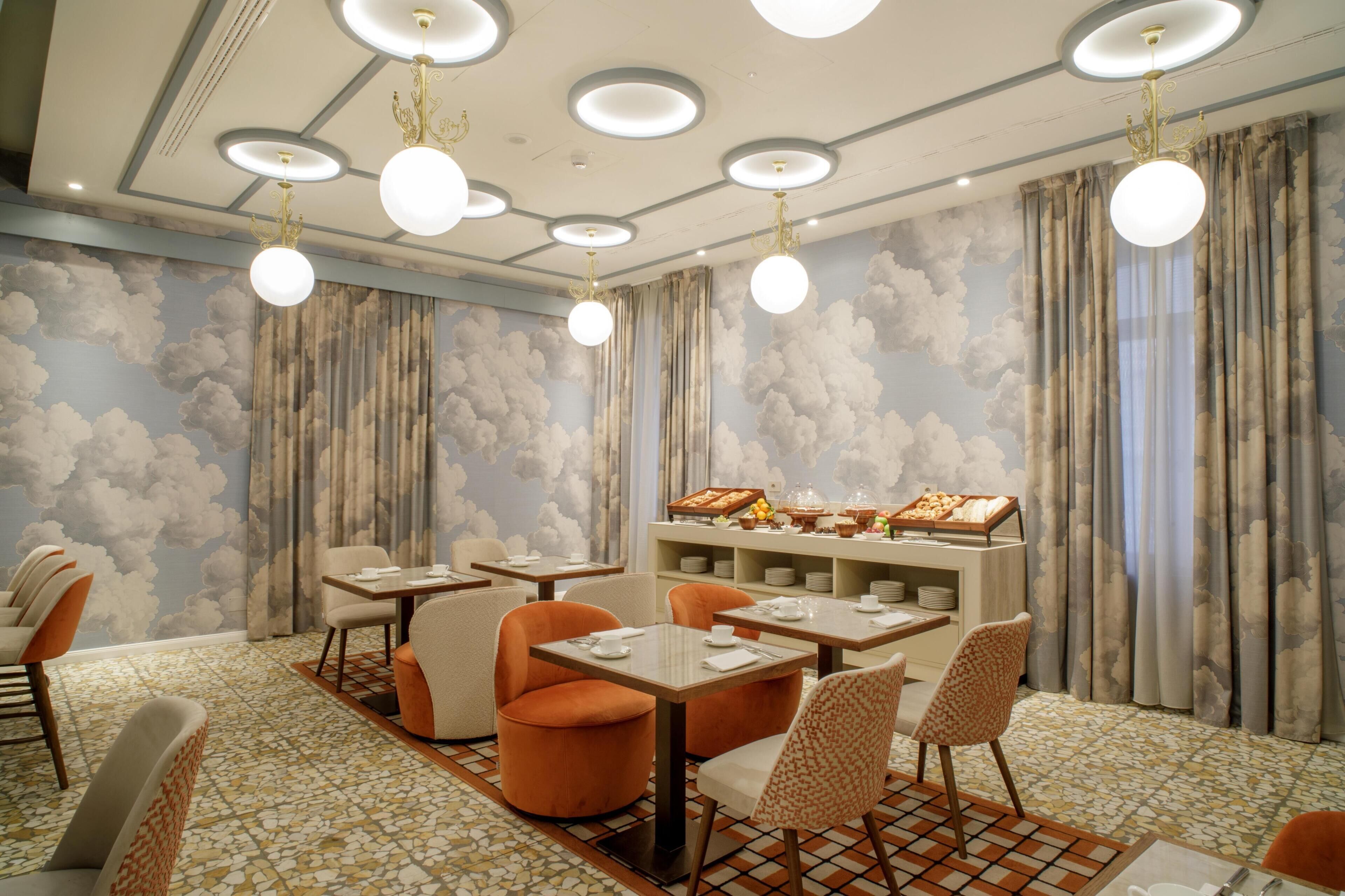 A dining area with round tables, chairs, and a buffet with various food items.