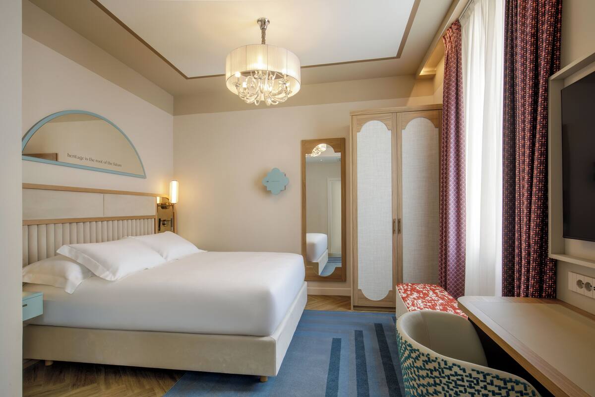 A hotel room with a bed, a desk, a TV, a wardrobe, and a mirror.