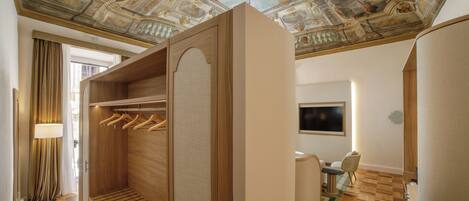 A hotel room with a wooden wardrobe, a ceiling with frescoes, a television, and a dining area.