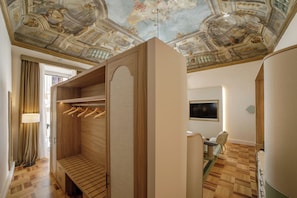 A hotel room with a wooden wardrobe, a ceiling with frescoes, a television, and a dining area.