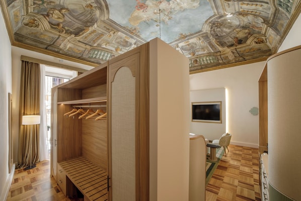 A hotel room with a wooden wardrobe, a ceiling with frescoes, a television, and a dining area.