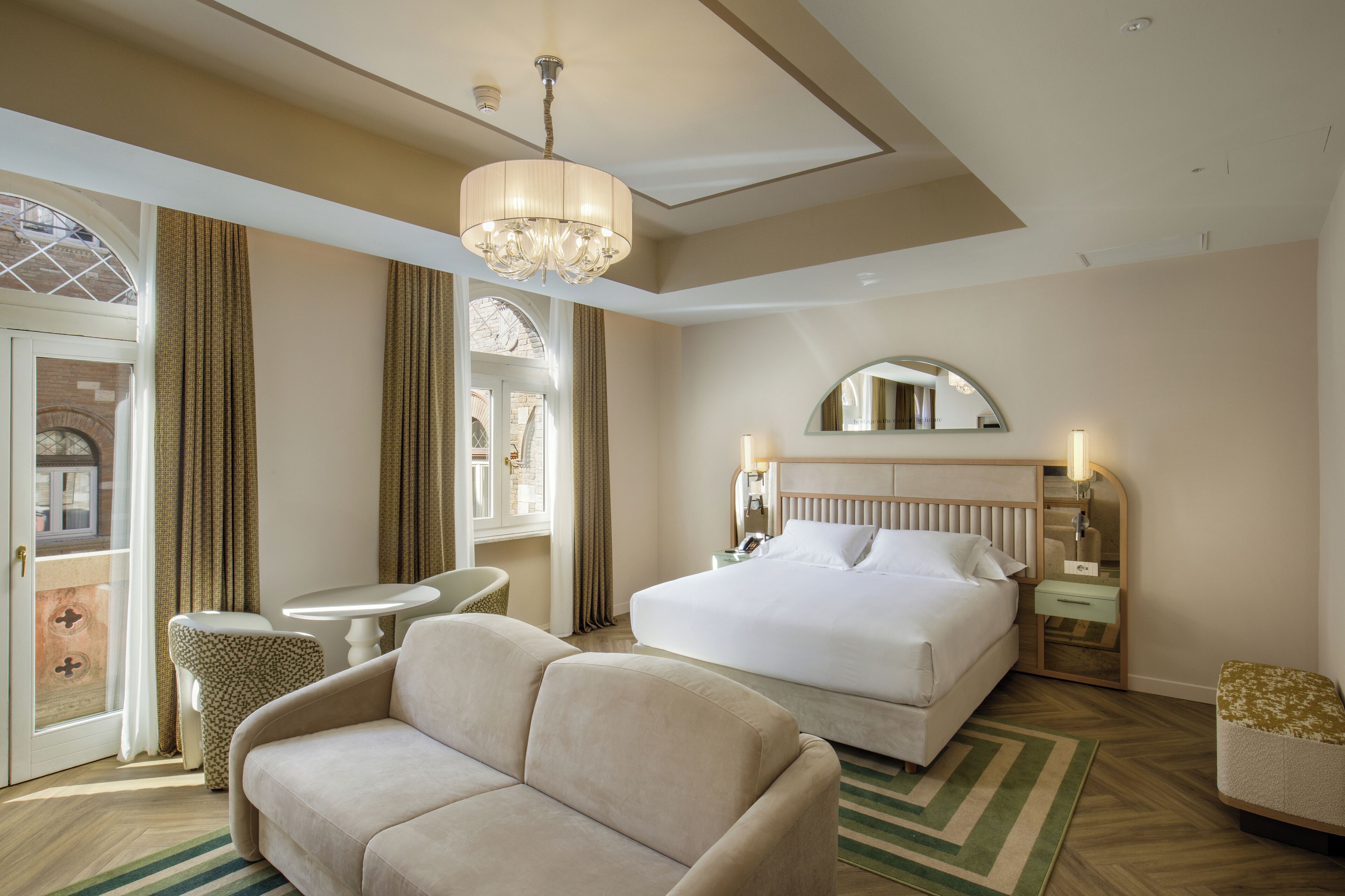 A hotel room with a large bed, a sofa, a small table, and a chandelier.