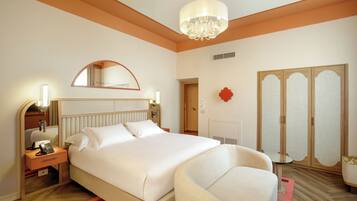 A hotel room with a bed, bedside table, lamp, mirror, wardrobe, and a chandelier.