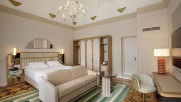 Une chambre d’hôtel comprenant un lit, un canapé, une petite table, une chaise, une armoire, un miroir et un lustre.