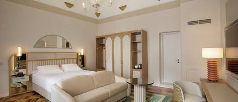 Habitación de hotel con cama, sofá, una mesita, una silla, armario, espejo y candelabro.