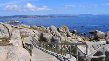 Una passerella di legno che conduce a una costa rocciosa, con vista chiara sul mare e montagne lontane.