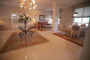 A hotel lobby with a round table, chairs, a sofa, and a chandelier.