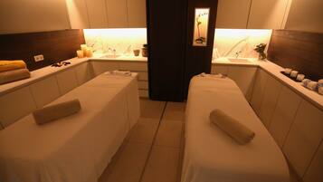 A spa room with two massage tables, a sink, and a mirror.