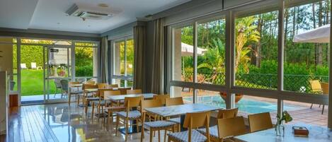 Un comedor amplio con grandes ventanales que ofrecen vistas a una piscina y zonas verdes.