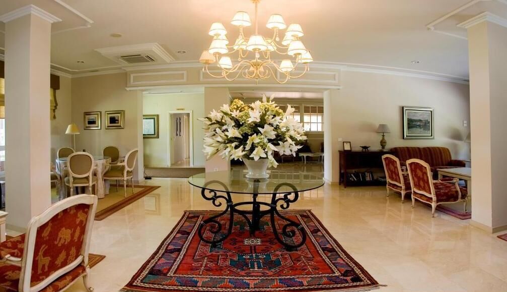 A spacious living room with a glass-top coffee table, a chandelier, and a floral centerpiece.