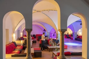 Un hall de hotel con asientos rojos, una zona de bar y un mostrador de recepción.
