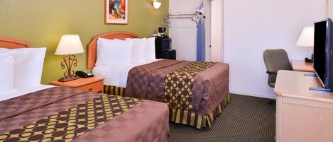 A hotel room with two beds, a desk with a television, a chair, a desk lamp, a nightstand with a phone, and a wall-mounted hairdryer.