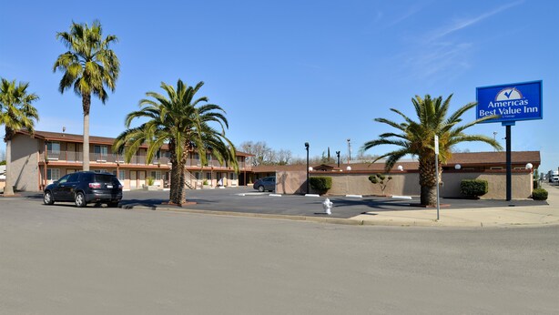 A Best Value Inn with a clear blue sky, palm trees, and a parking lot with a car.