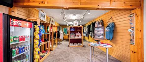 A store with shelves of snacks, a Coca-Cola cooler, and racks of clothing.