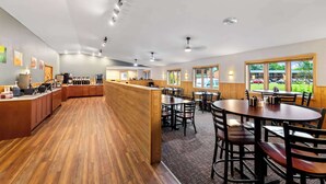 A spacious restaurant with wooden flooring, a central counter, and multiple dining tables and chairs. - Quality Inn & Suites Munising (Munising)