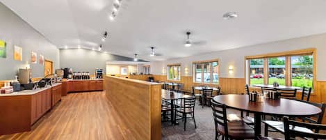 A spacious restaurant with wooden flooring, a central counter, and multiple dining tables and chairs.