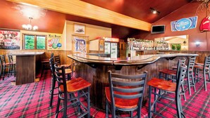A bar area with wooden bar counters, red plaid carpet, and multiple stools. - Quality Inn & Suites Munising (Munising)