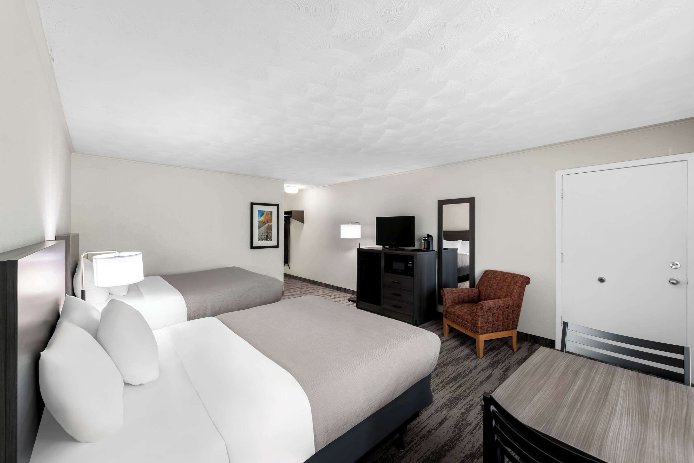Une chambre d’hôtel avec deux lits, un bureau, une chaise, une télévision et une armoire.