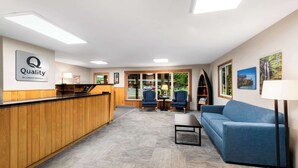 A hotel reception area with a wooden reception desk, two armchairs, a sofa, and a lamp. - Quality Inn & Suites Munising (Munising)