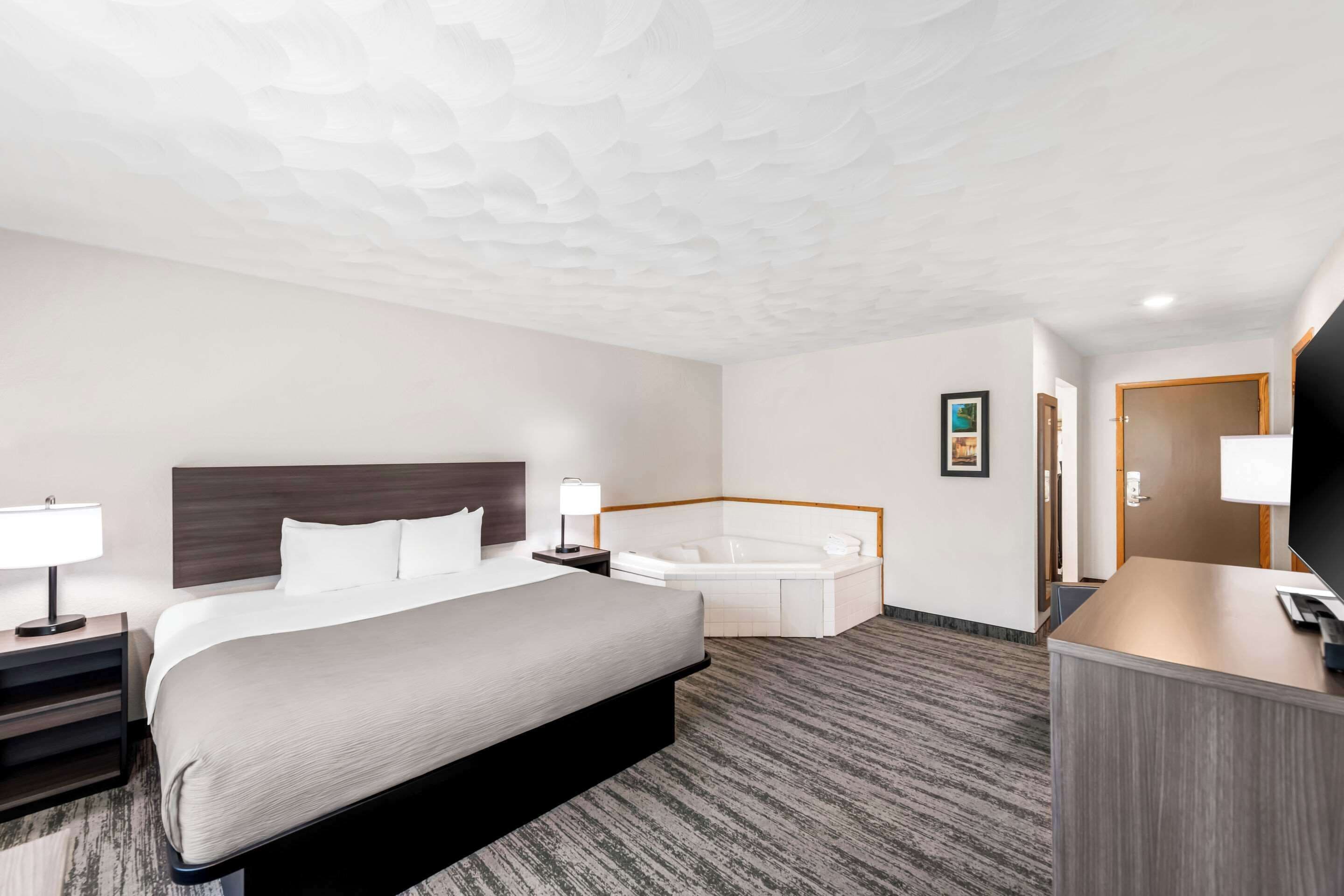 Ett hotellrum med en stor säng, ett separat badrum med badkar, ett skrivbord och en reception.
