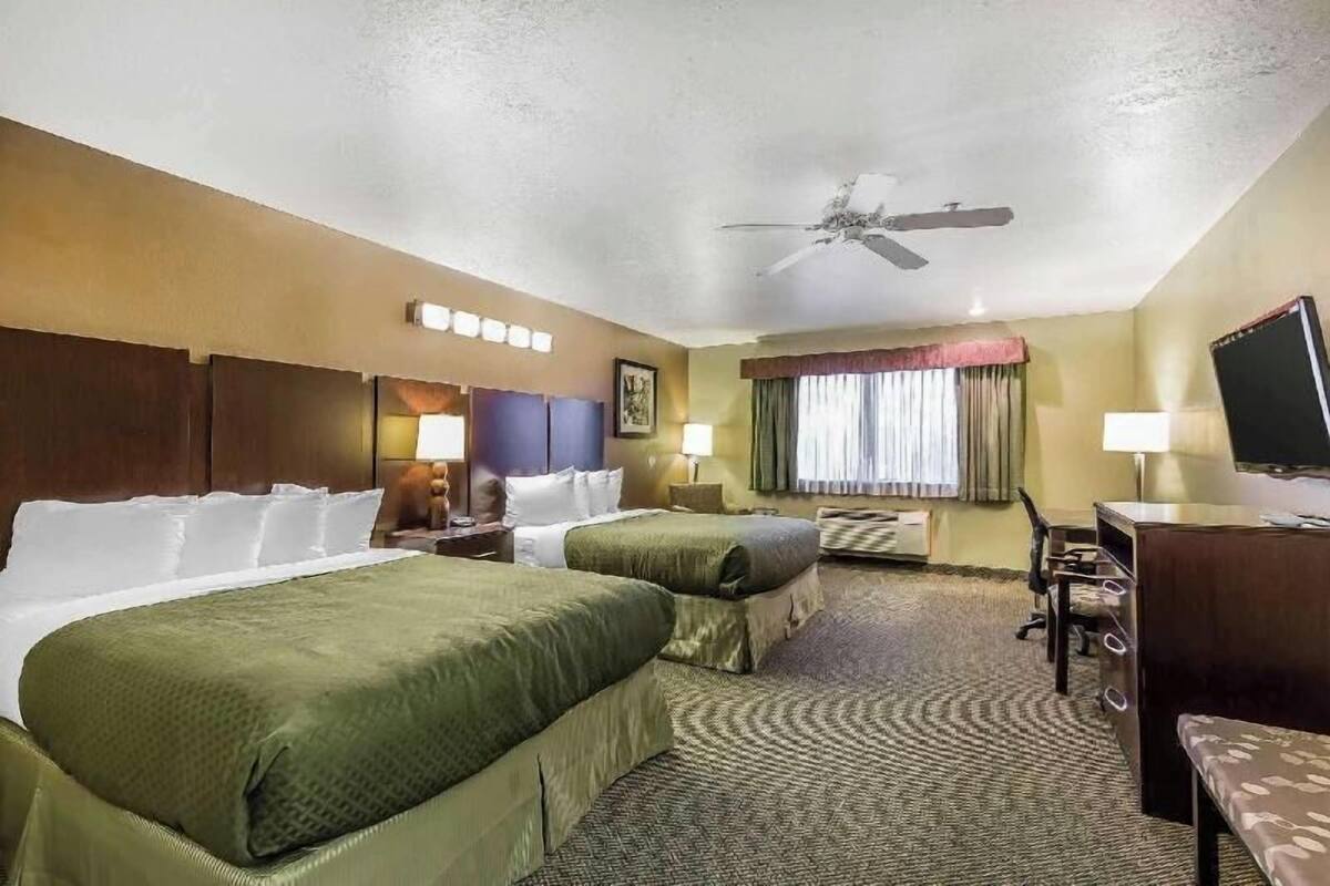A hotel room with two beds, a desk, a chair, a television, and a ceiling fan.