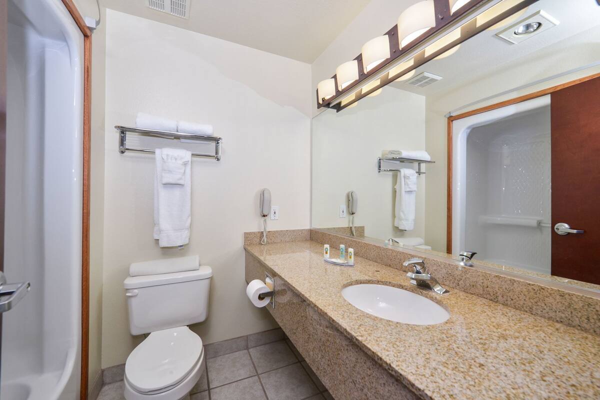 A bathroom with a toilet, sink, mirror, towel rack, and a shower door.