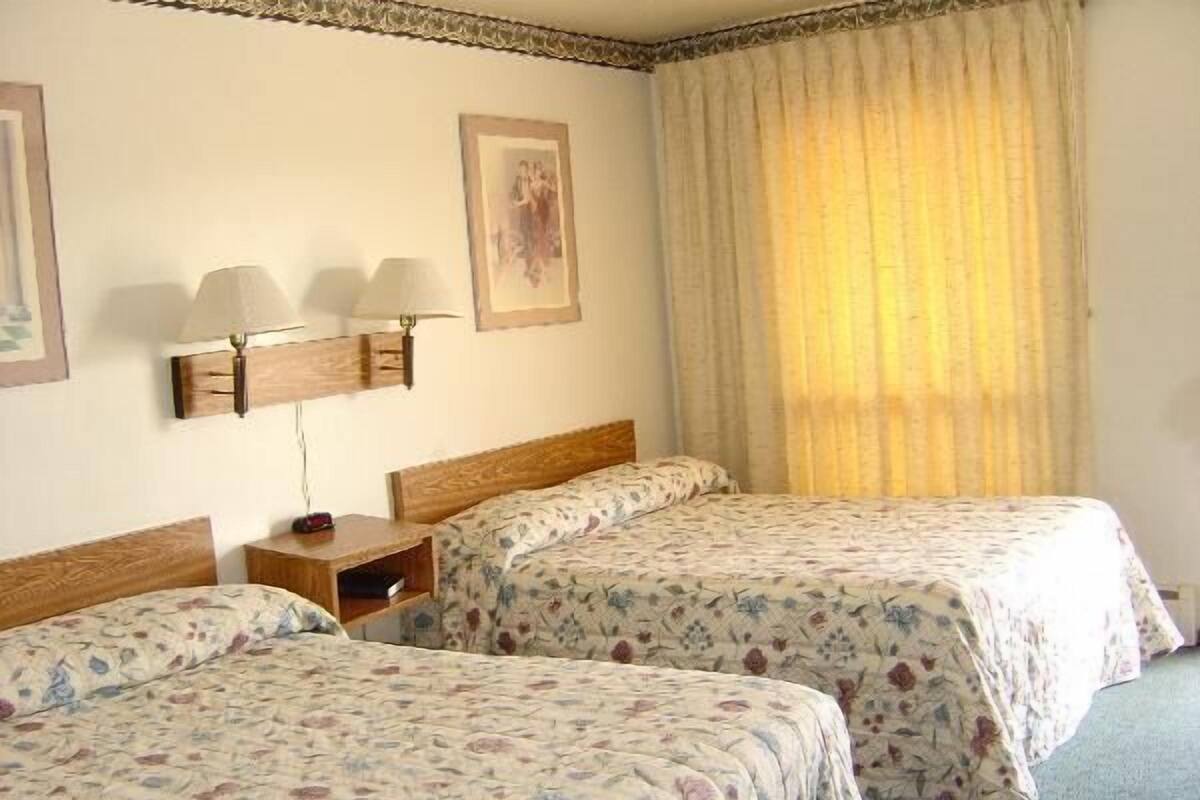 Ein Hotelzimmer mit zwei Betten, einem Nachttisch, einer Lampe und einem gerahmten Bild an der Wand.