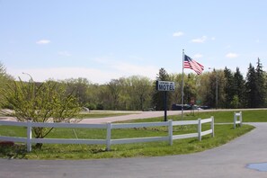 Une enseigne de motel avec un drapeau américain, une clôture blanche et une route où circulent des véhicules.