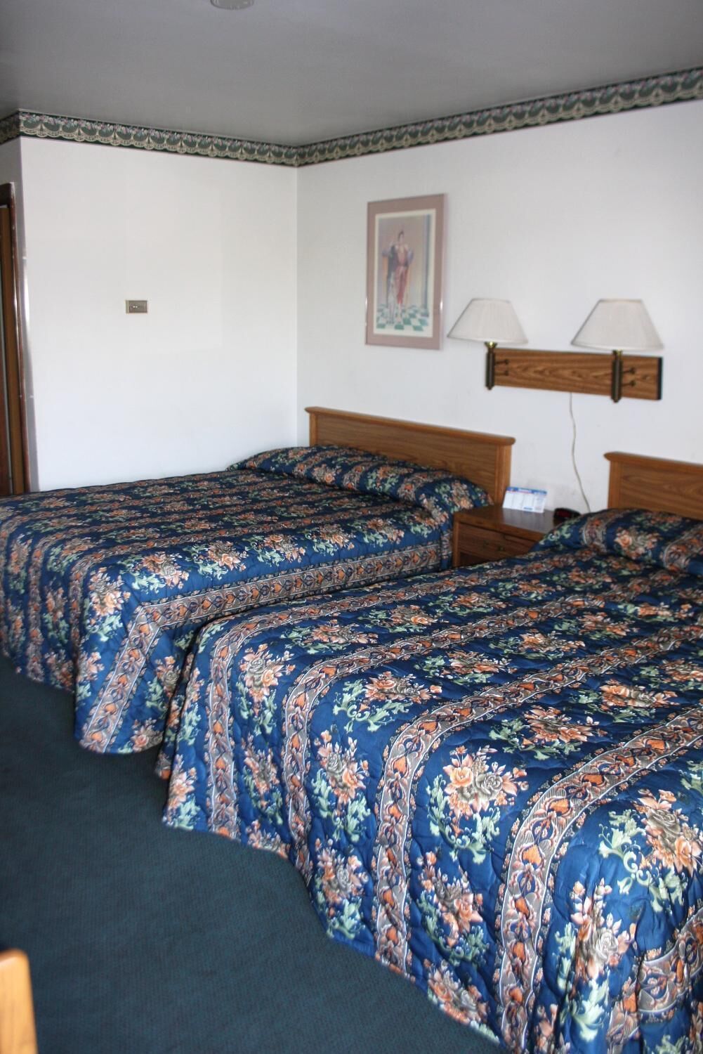 A room with two wooden beds, each with floral-patterned bedding. There are two wall-mounted lamps on either side of the beds.