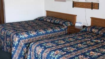 A room with two wooden beds, each with floral-patterned bedding. There are two wall-mounted lamps on either side of the beds.
