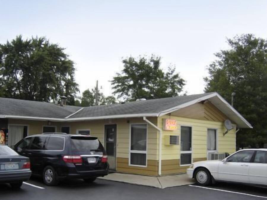 A motel with a single-story structure, a small attached garage, and a neon sign indicating a restaurant.