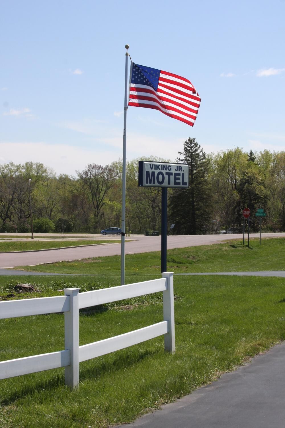 A motel sign with an American flag, a white fence, and a road in the background.