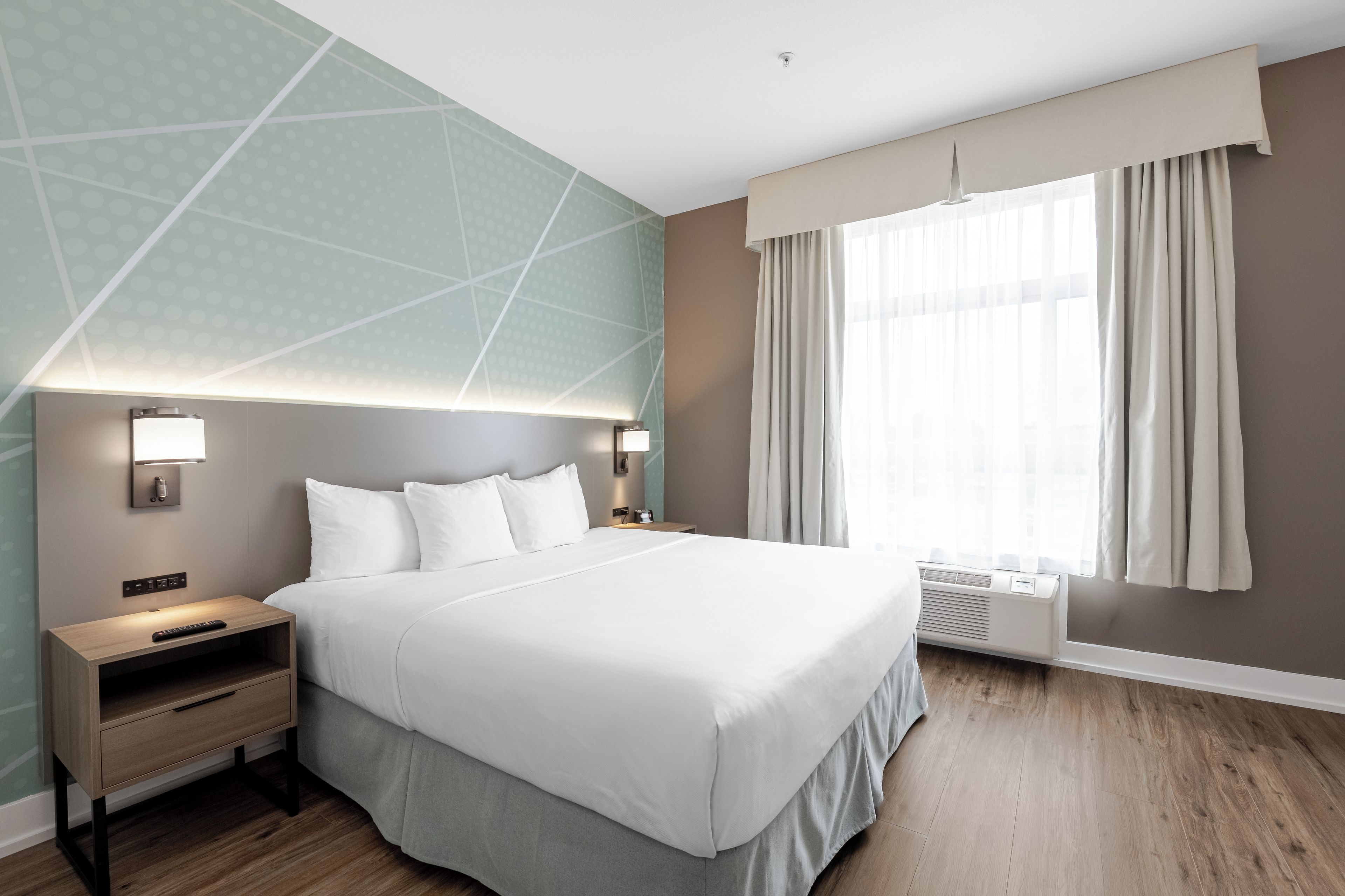 Een hotelkamer met een groot bed, nachtkastjes, een wandlamp, een raam met gordijnen en een plafondlamp.