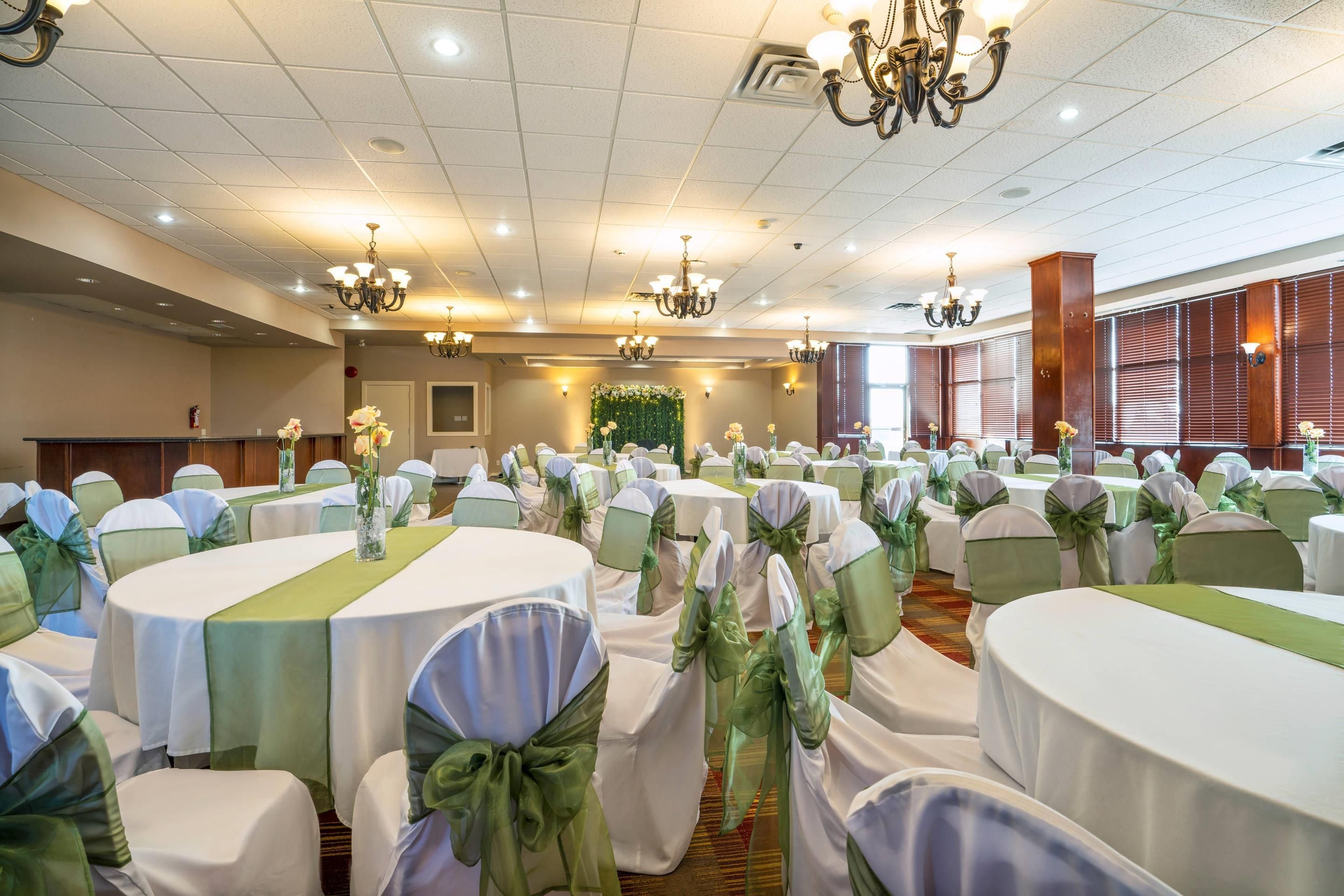 A banquet hall with round tables, green sashes, and chandeliers.