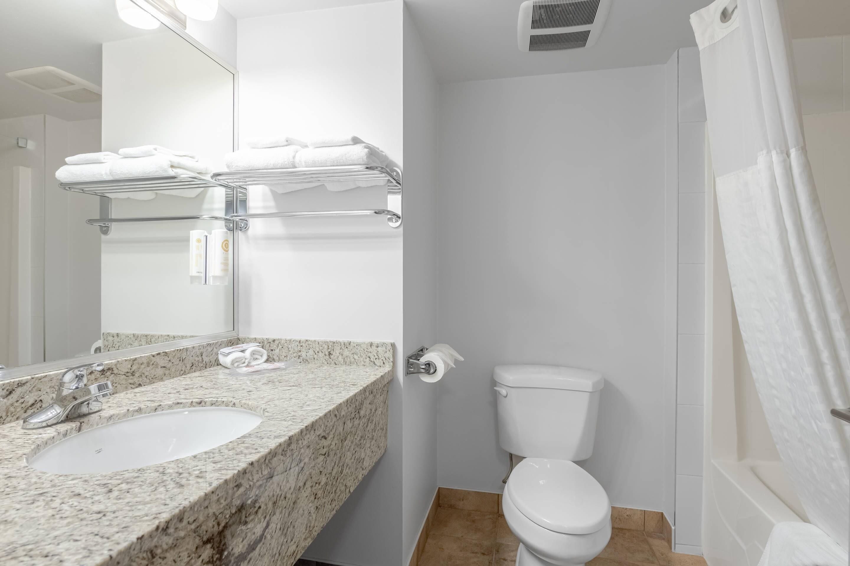 Un baño con lavamanos de granito, inodoro y toallero con toallas dobladas.