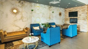 A modern lobby with a marble wall, blue armchairs, a sofa, and a TV mounted on a brick wall.