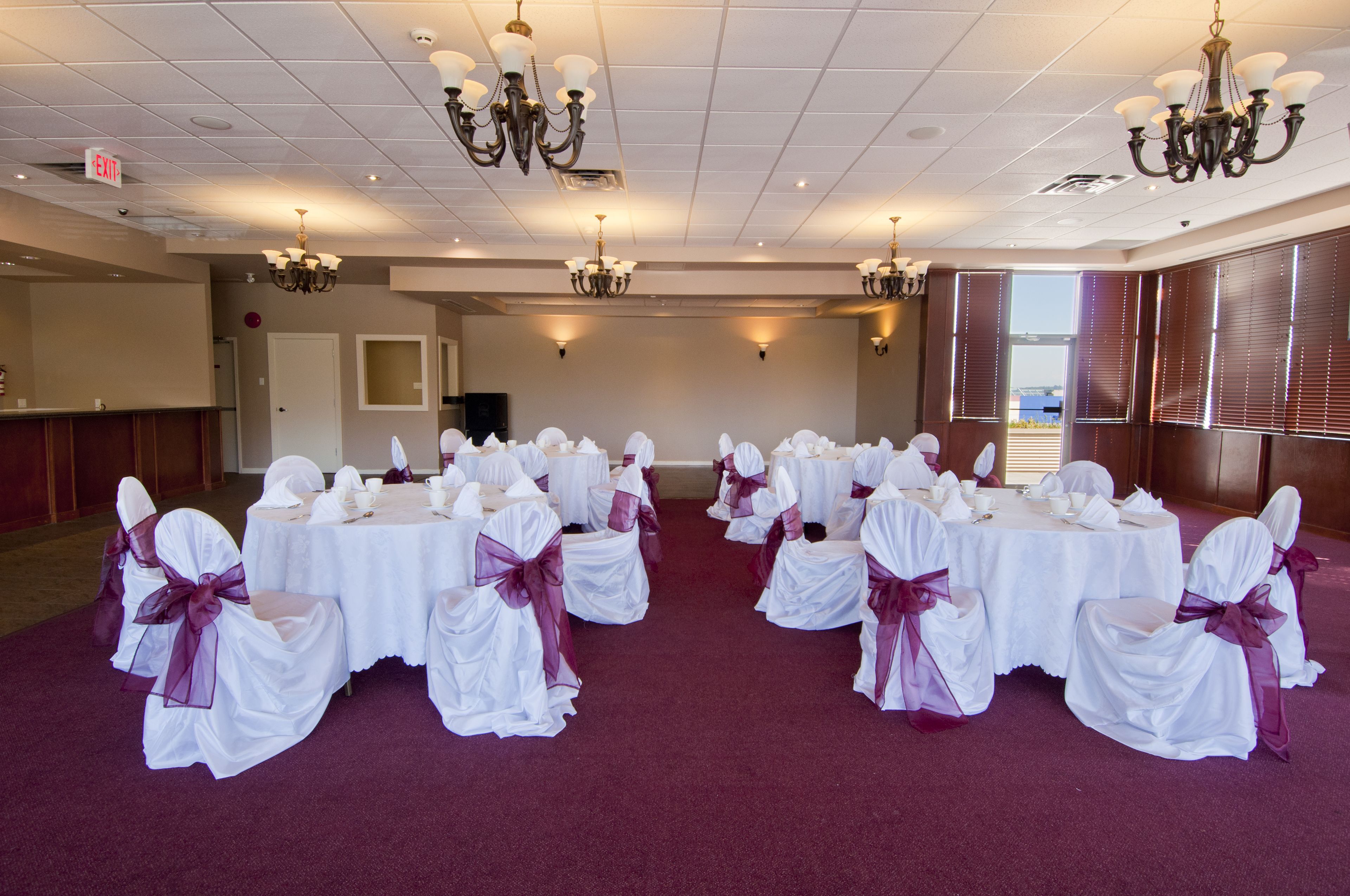 A banquet hall with round tables and chairs, chandeliers, and a red carpet.