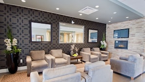 A modern lounge area with multiple sofas and armchairs, a large mirror, and a flat-screen TV mounted on the wall.