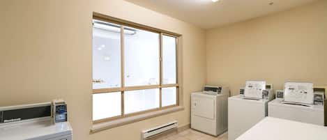 A laundry room with a large window, two washing machines, and a dryer.