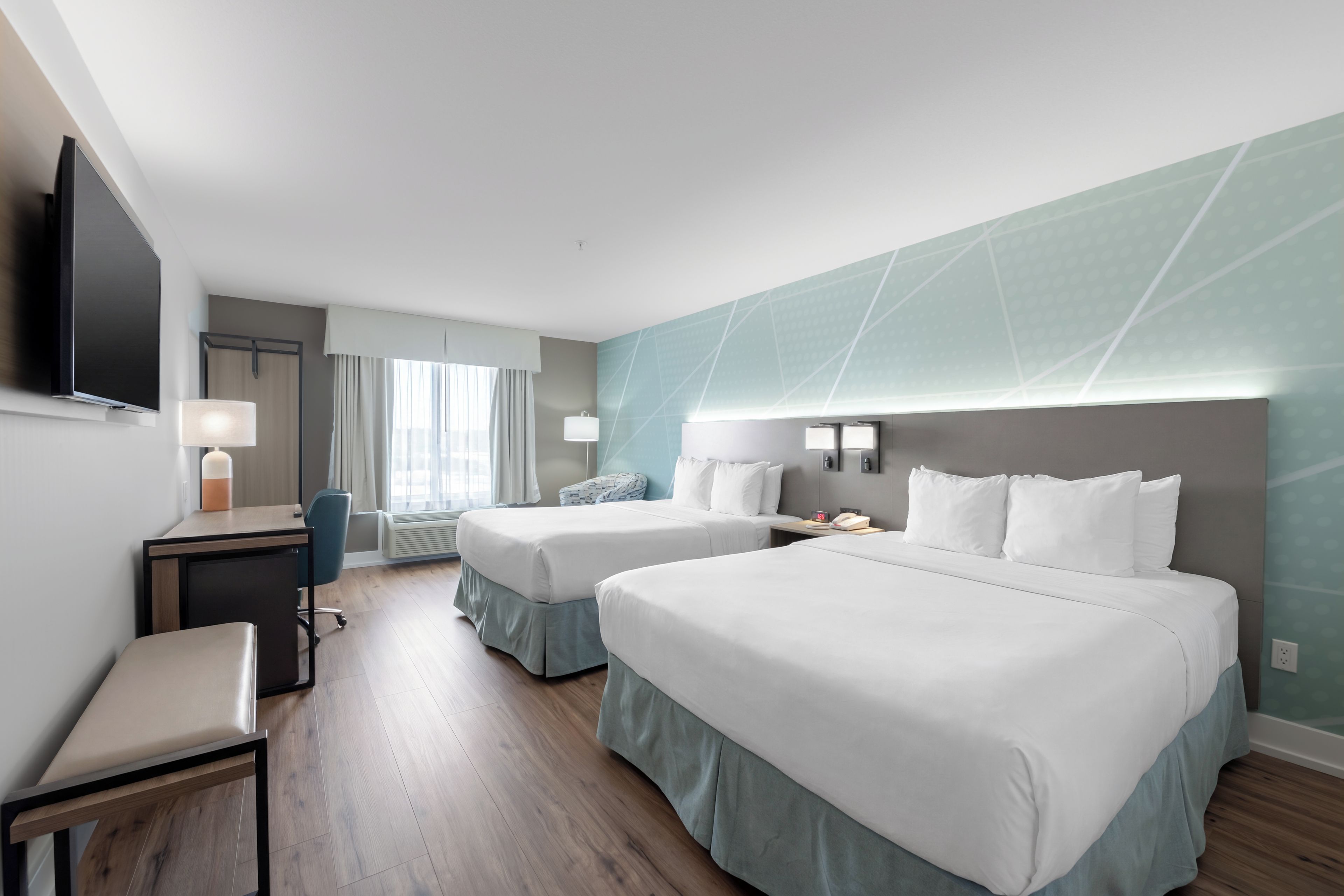 A hotel room with two beds, a desk, a chair, a TV, and a window with curtains.