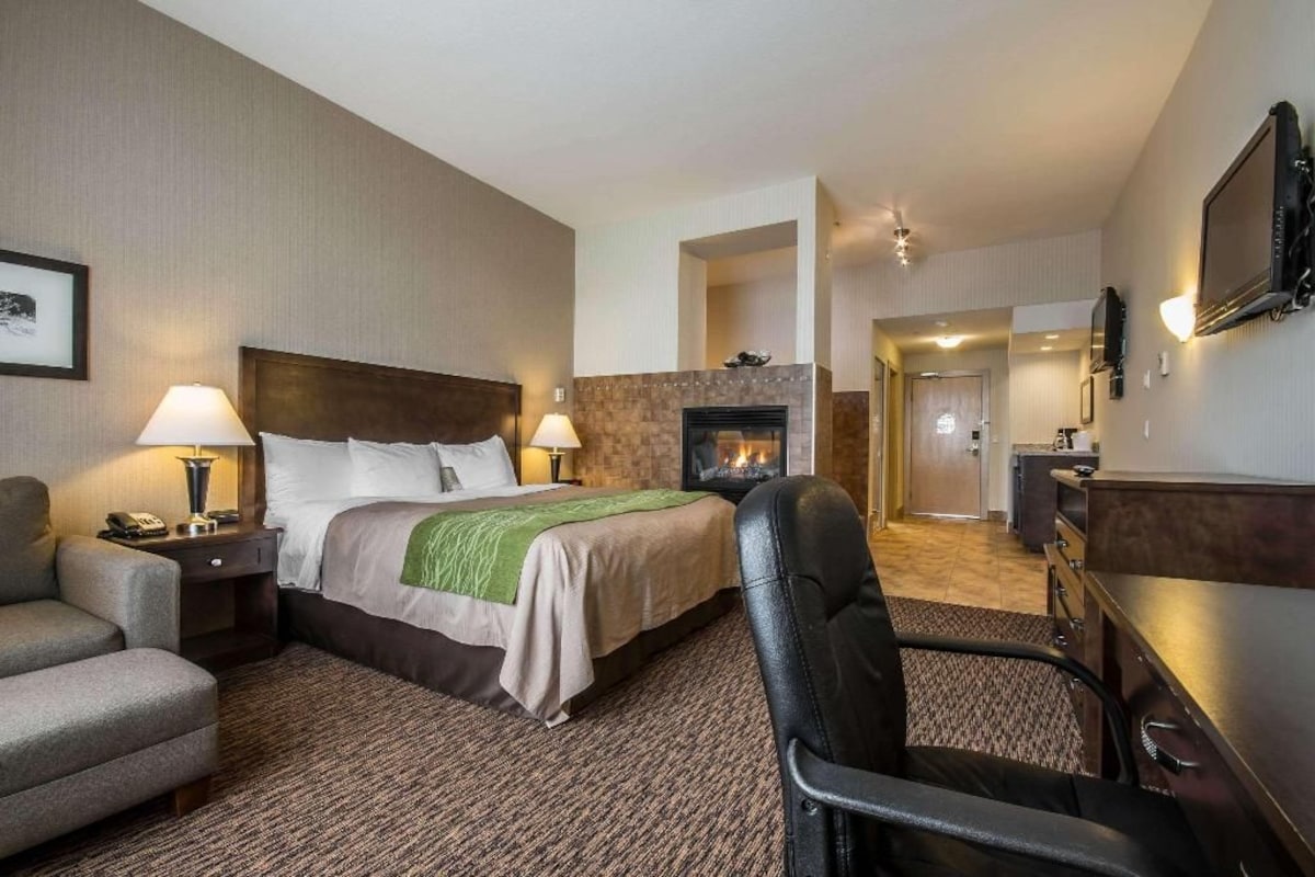 A hotel room with a bed, a chair, a desk, a fireplace, and a television.