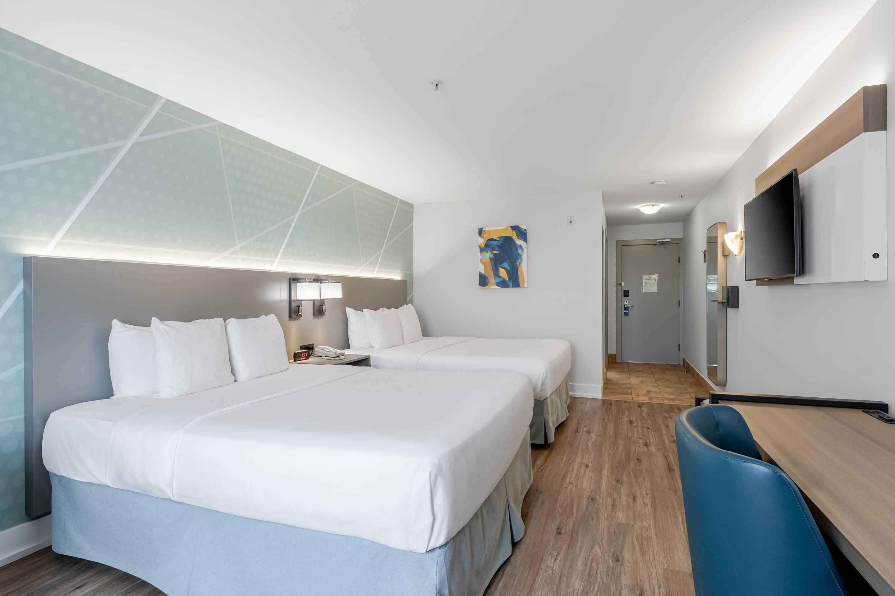 Habitación de hotel con dos camas, un escritorio, una silla, un televisor y un cuadro en la pared.