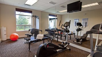 Un gimnasio con equipo de ejercicio, un espejo grande y ventanas que dan a árboles.
