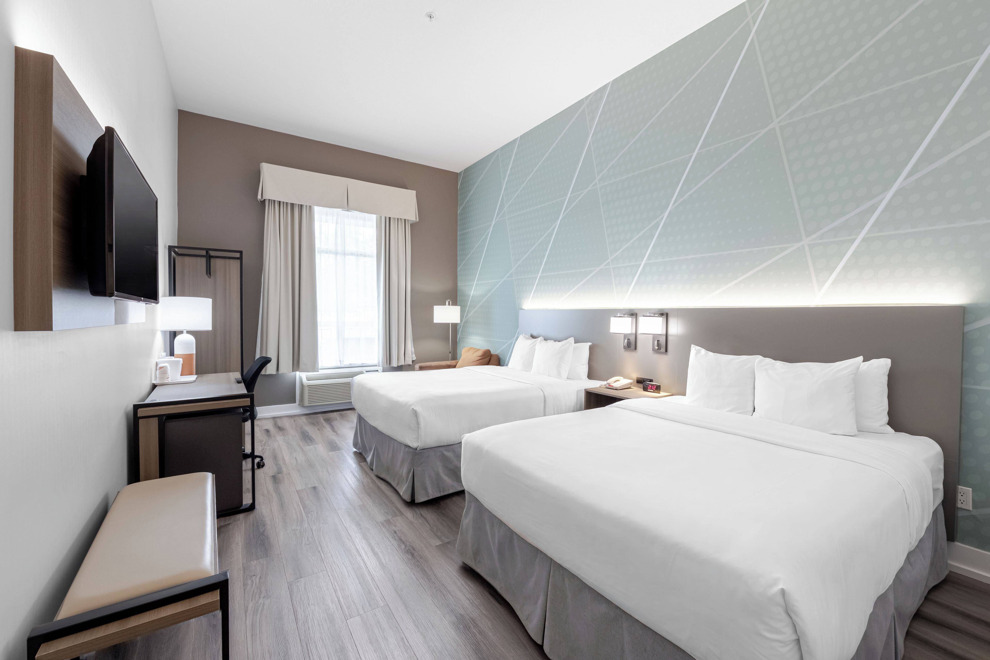 Een hotelkamer met twee bedden, een bureau, een stoel, een televisie en een raam met gordijnen.