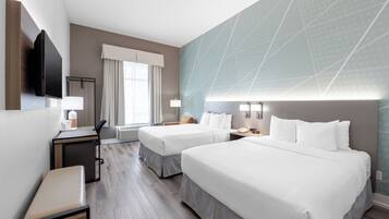 Een hotelkamer met twee bedden, een bureau, een stoel, een televisie en een raam met gordijnen.